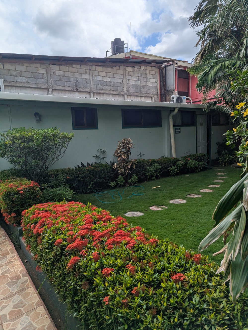 Jardín del Hostal Della Nonna, con camino de piedras y flores rojas